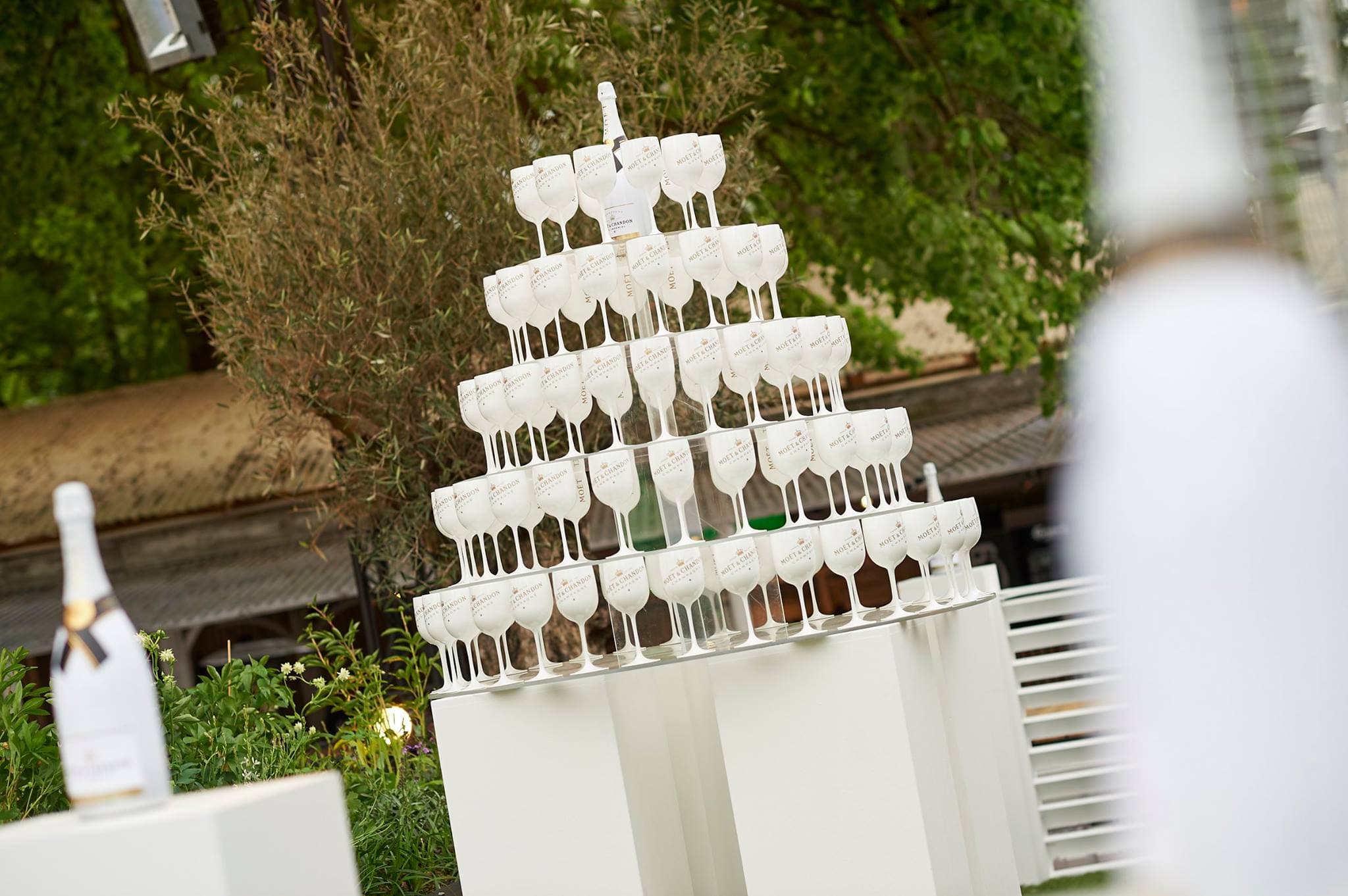 A tower of champagne coupes stacked on a plinth in a garden