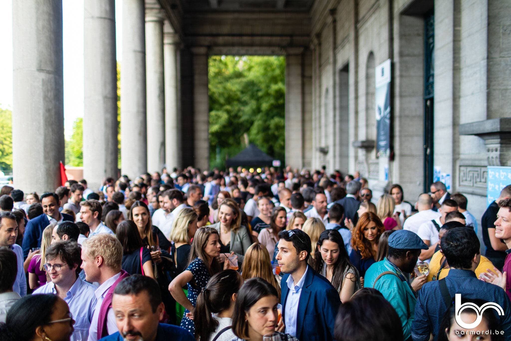 A crowd filling a stone colonnade on a summer evening