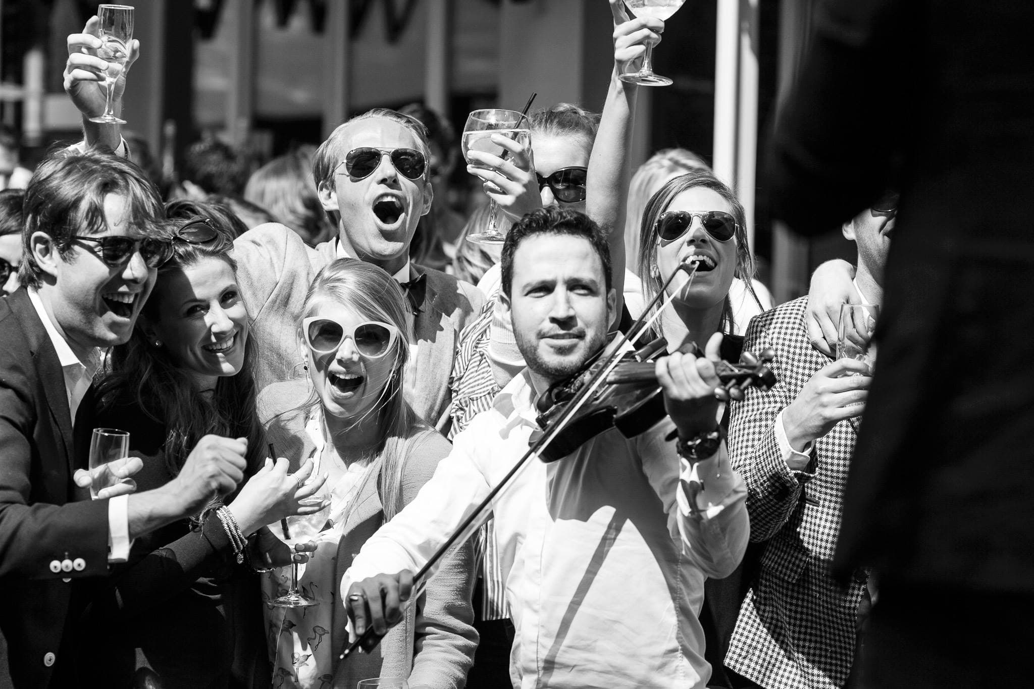 Guests raising their glasses beside a violinist playing in the sun